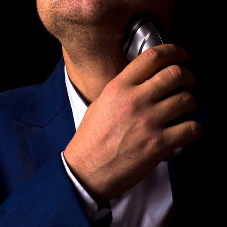 A man in a suit shaves with an electric razor. Preparation for a business meeting. Daily ritual for...