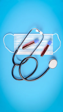 Stethoscope, protective face mask and test tubes with blood on a blue background.