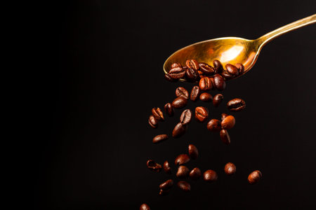Roasted coffee beans falling from a spoon on a black background.