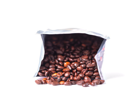 Coffee beans spilling out of packaging on a white background.