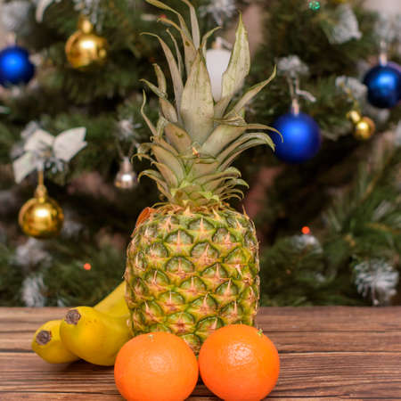 New Year and Christmas. Tropical fruits on a wooden table. Tangerines, bananas and pineapple on a wooden background opposite the Christmas tree.の写真素材