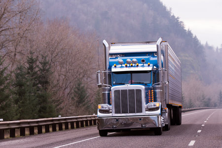 Blue classic semi truck with trailer and orange lights on the hiway