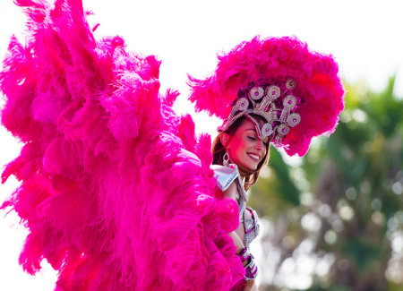 A participant in the Brazilian festival festival dress with multicolored feathers, blown by the wind, and the decorations on the background of green treesのeditorial素材