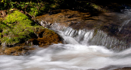 Creek flowing over rocks overgrown with green mossの写真素材