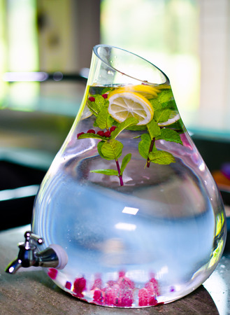 Appetizing refreshing healthy drink made from cranberries, mint, lemon slices, raspberries and water in a large glass container with craneの写真素材