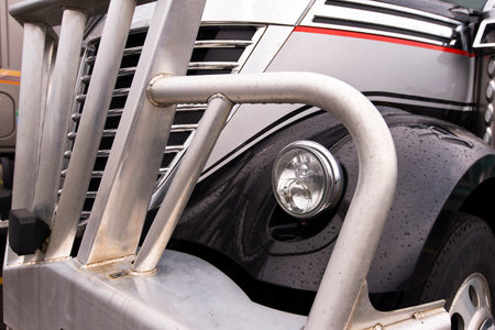 Detail of the front of a modern dark semi truck, including the hood, chrome grille, headlamp, wing...