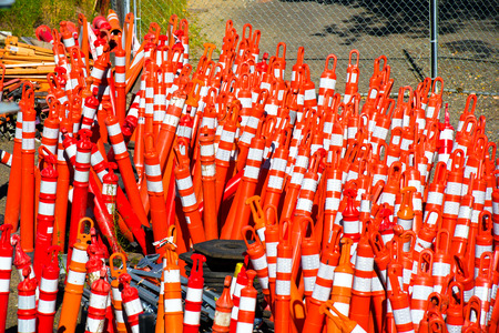 Storage area with lots of bright orange traffic restrictive precautionary plastic columns with white stripes and a loop at the top.  Security features of construction work and traffic の写真素材