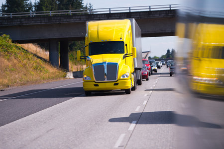 Bright modern showy yellow truck with trailer carrying cargo on the highway in front of the other cars. の写真素材