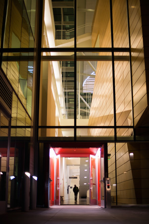 The man at the entrance to the open doors of a multi-storey modern building with red trim modern look of architecture in the evening in the lobby with the included lighting.の写真素材