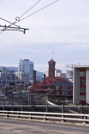 The train station with a tower and buildings under the red-tiled roofs and access rails surrounded by modern buildings with contemporary architecture skyscrapers on streets modernistic city with roads with a security fence and power line.の写真素材