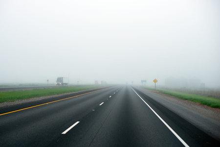 The convoy of semi trucks of various models and brands on the milk fog-drenched straight interstate highway line separated oncoming traffic going into the horizon hidden veil of mist.の写真素材