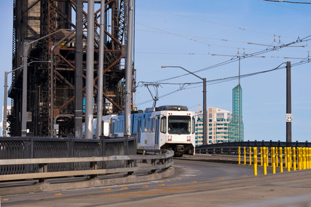 Modern white streetcar and power lines on the turn from the old drawbridge with rusty farm across the river Willamette in Portland Down Town on the background of modern office buildings of concrete and glass.のeditorial素材