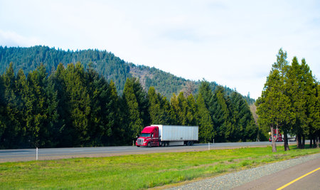 Red powerful modern professional semi truck to haul dry van trailer on the interstate highway with...