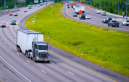 A broad highway with a dividing strip of grass opposite sides with a classic semi truck traffic and...