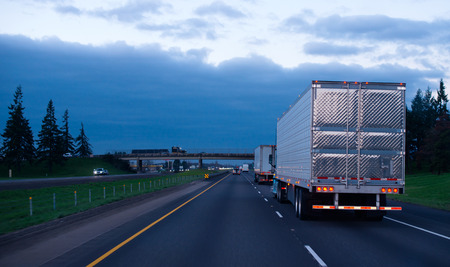 The convoy of semi trucks with reefer trailers on flat like an arrow evening road の写真素材