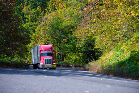 Professional red big rig semi truck with refrigerated trailer rides up the hill on the scenic...
