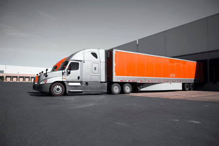 Two modern professional commercial semi trucks in gray and orange with dry van trailers are standing...