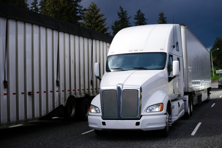 Modern American production bonneted model white big rig semi truck transports in a covered trailer dry packaged goods along the highway traffic surrounded by other road vehicles.のeditorial素材