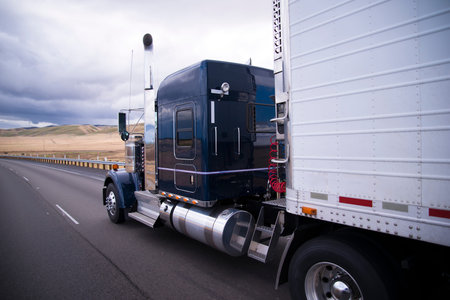 Classic bonneted American semi truck with chrome trim and a refrigerator trailer drive on the straight road in the California fields.の写真素材