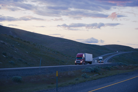 Evening winding road in the hills of Columbia Gorge with moving semi trucks on the highway hurrying to complete the delivery before darkness.の写真素材