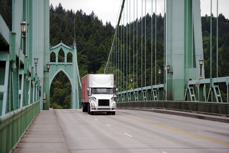 Semi Truck with a box trailer moving on the picturesque gothic riveted metal bridge with arches and cable extensions. St. Johns Bridge is located in Portland Oregon and is a local landmarkの写真素材