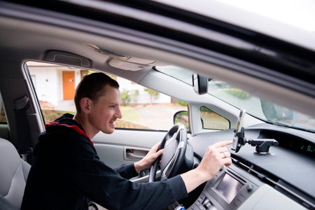 A young male driver with a smile and good mood adjusts touch screen navigation on mobile phone while sitting behind the wheel of a modern luxury car to compile travel routesの写真素材