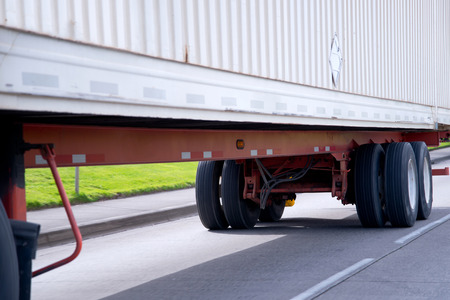 Wheels and chassis on orange frame of long commercial semi truck trailer mounted with a ribbed container for transport of dry industrial goods over long distances freights.の写真素材