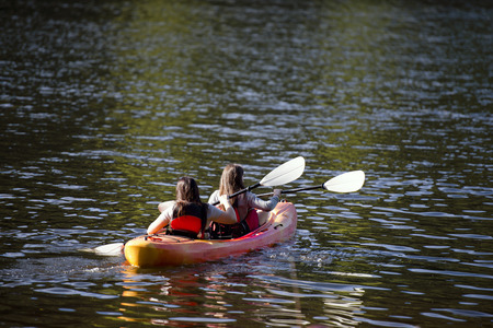 Young girls with oars rowing in the bright kayak on Trillium Lake, reflection of the sparkling green of the surrounding lake and forest patches of sunlight in shallow water wavy ripples - a great way to relax and devote their energies to the development oの写真素材