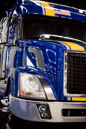 A shiny bright blue modern semi truck with a yellow stripe on the cab with a reflection of light on...
