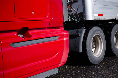 Fragment of red modern big rig heavy-duty local and long haul semi truck with day cab and dry van trailer carry commercial cargo for delivery to destination warehouse by the wide interstate roadの写真素材