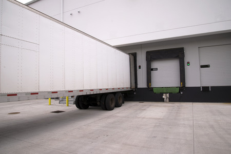 Long full-sized semi trailers stand it row at the dock gates of a large industrial warehouse loading and unloading the delivered goods and cargo that will be delivered after loading.の写真素材