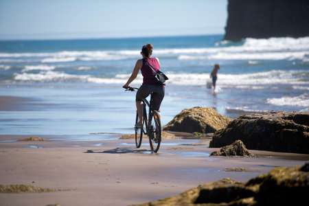 A woman with a beautiful figure looks great due to cycling along the shore of the Pacific Ocean, slowly rolling her waves onto the gently stony shore, refreshing him with a light breezeの写真素材