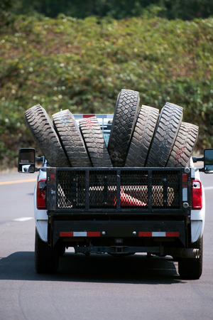 A large pickup truck transport used tires with large tread pattern for big rig semi trucks in its dump moving along a picturesque roadの写真素材