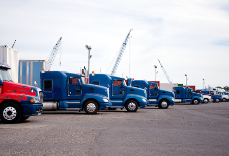 Bonnet semi trucks of different colors, models and designs for different uses for the purpose with different trailers are parked in row in anticipation of loading in an industrial production parkの写真素材