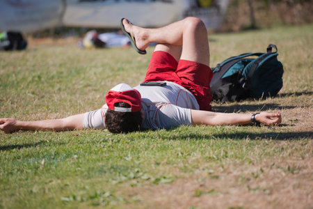 A young man in a T-shirt and shorts sunbathing in the sun lying on the grass and hands spreading...