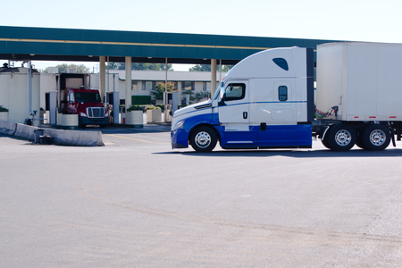 Long haul big rig semi truck with dry van trailer going on truck stop to gas station with another semi trucks for refueling tanks for the continuation of the delivery of goodsの写真素材