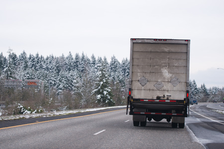 Powerful middle size white day cab American made big rig semi truck with box cargo dry van trailer transporting industrial cargo and running on the wide multiline highwayIn winter snow weatherの写真素材