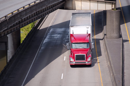 Big rig red American semi truck transporting commercial cargo in covered dry van semi trailer going...