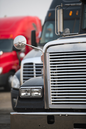 Big rigs semi trucks of different brands models and colors are lined up in parking lots truck stops rest areas filling vacant places to rest have lunch or wait for cargo following traffic scheduleの写真素材