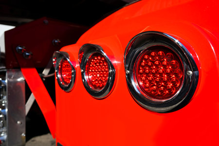 Line of rear round red marker lights with chrome rims on fender of red big rig semi truck shining on...