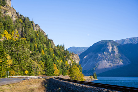 Autumn landscape with turning highway and railway along the Columbia River with a river on one side and a rocky mountain covered with autumn trees on the other side of the roadsの写真素材