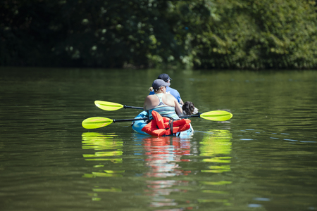 A man and a woman husband and wife with a big dog are kayaking on the lake Lacamas in the green forest, actively moving and relaxing at a hot summer day and love healthy lifestyleの写真素材