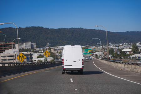 White popular compact comfortable commercial useful economical small business or cargo delivery mini van running on the wide highway in industrial area of urban city to point of destinationの写真素材