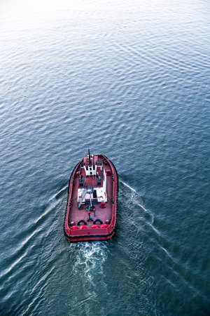 The small red workhorse tugboat surrounded with rubber tires and covered cabin with crew of sailors...