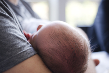 A newborn baby with black hair sleeps peacefully and sweetly in the arms of the father, with infant trustfulness clinging to it, as if feeling in it protection against any adversities and dangersの写真素材
