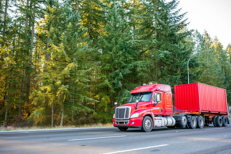 Red big rig day cab classic American idol bonnet semi truck with vertical exhaust pipes transporting...