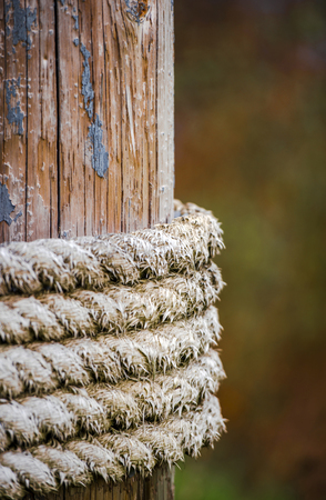 Powerful thick old braided natural hemp ship rope, strayed from long time to use, is wound by rings on wooden mooring pole as a symbol of strength, reliability and stability.の写真素材