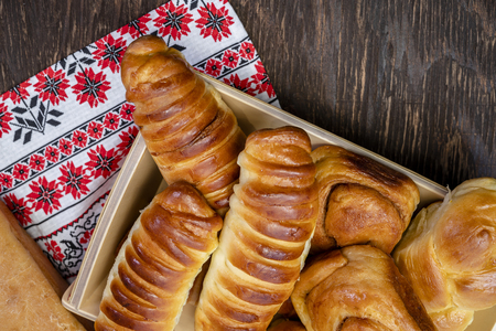 Appetizing delicious ruddy glazed baked buns, pies and pastries with cinnamon and various fillings, made from premium organic flour, laid out on a wooden plate as a dessert for coffee or teaの写真素材