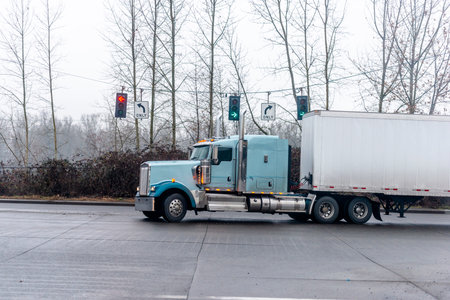 Big rig American classic long haul semi truck with dry van semi trailer turning on traffic light...