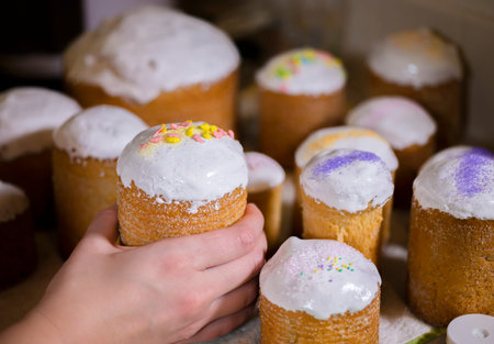 Baker decorates the upper part of Easter cakes covered with white sugar icing by colored granulated...